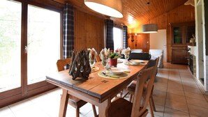 A wooden interior with a dining table set for four, a large window, and a kitchen area. - Peaceful Holiday Home in Tenneville near Forest (Tenneville)