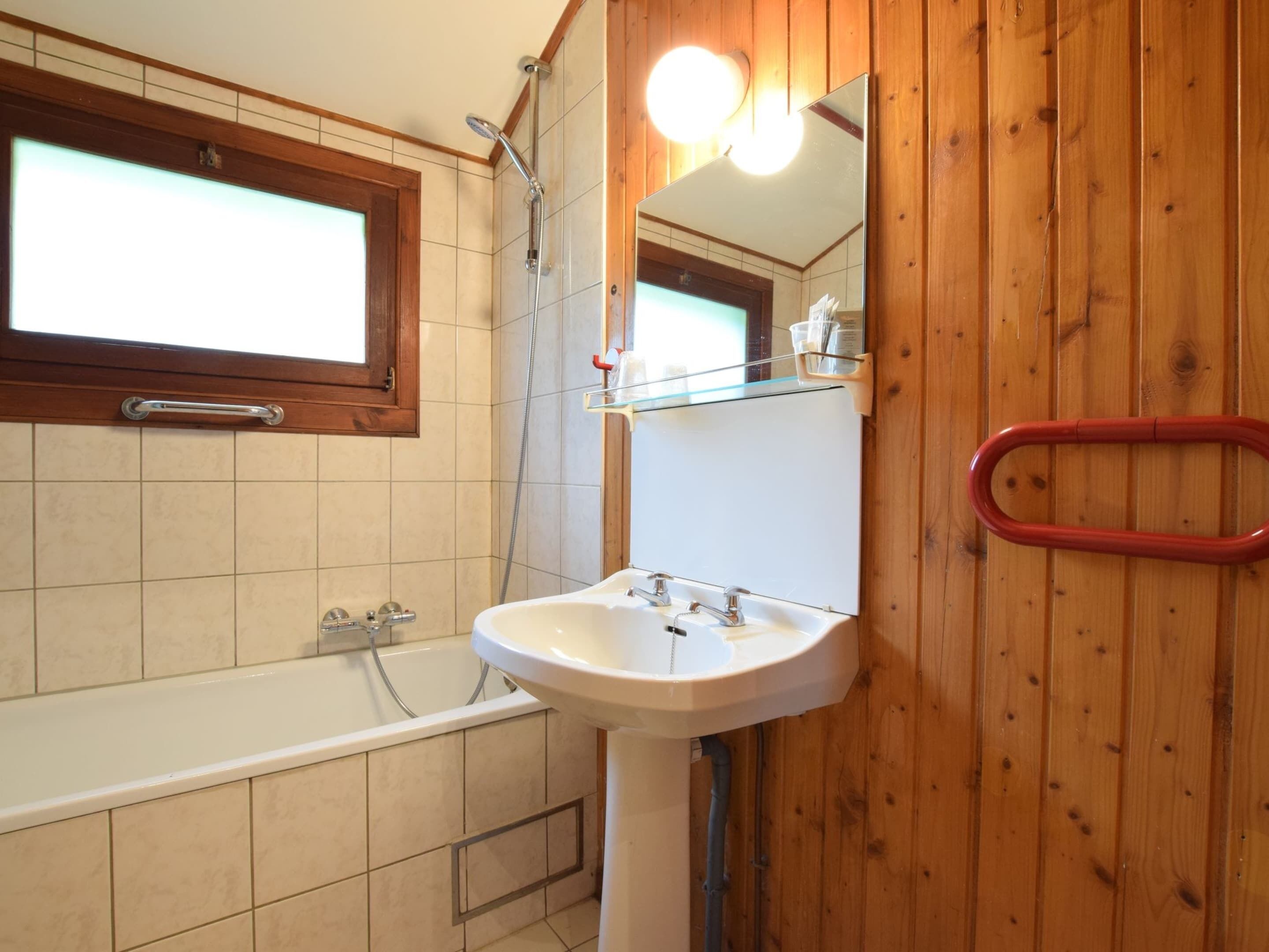 Un baño con bañera, lavamanos, espejo y paredes de madera.