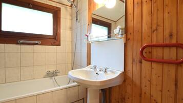 Un baño con bañera, lavamanos, espejo y paredes de madera.