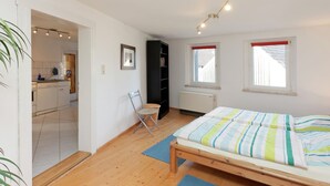 A bedroom with a bed, a window, a radiator, a chair, and a kitchenette in the adjacent room. - Lovely First Floor Apartment on the Edge of Bode (Thale)