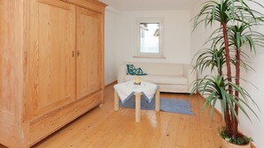 A room with a wooden wardrobe, a small table with a tablecloth, a white sofa, a window, and a potted plant. - Lovely First Floor Apartment on the Edge of Bode (Thale)