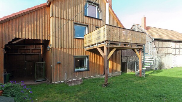 A wooden building with a sloped roof, a covered porch, and a fenced yard. - Lovely First Floor Apartment on the Edge of Bode (Thale)