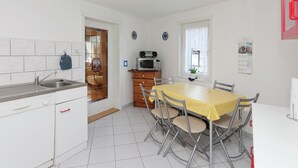 A compact kitchen with a sink, microwave, and wooden cabinets. A dining table with chairs is in the center, and a window with a plant is visible. - Lovely First Floor Apartment on the Edge of Bode (Thale)