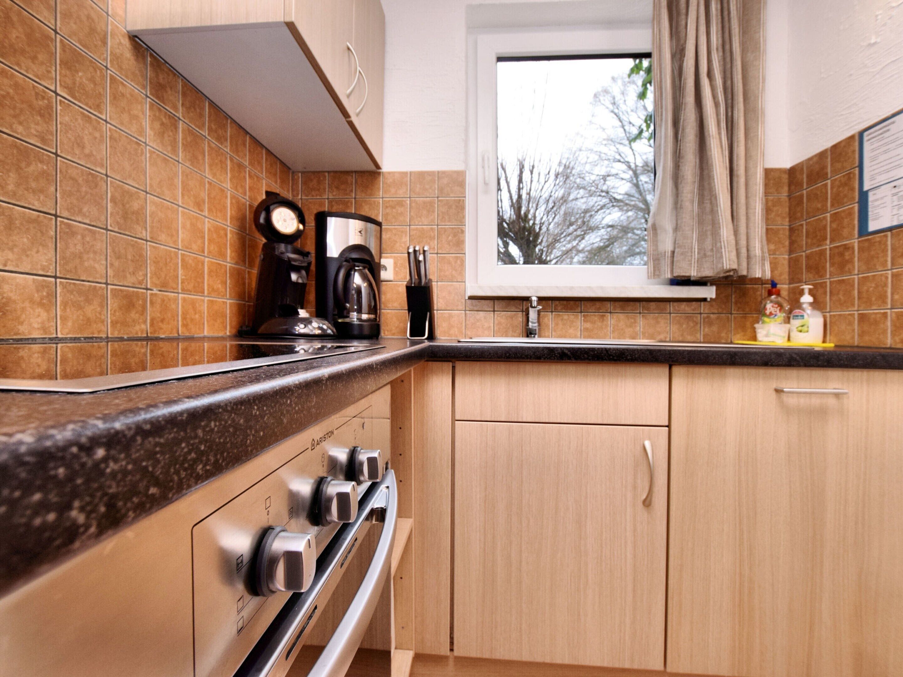 A kitchen with a stove, oven, and coffee maker. There is a window with a view of trees outside.
