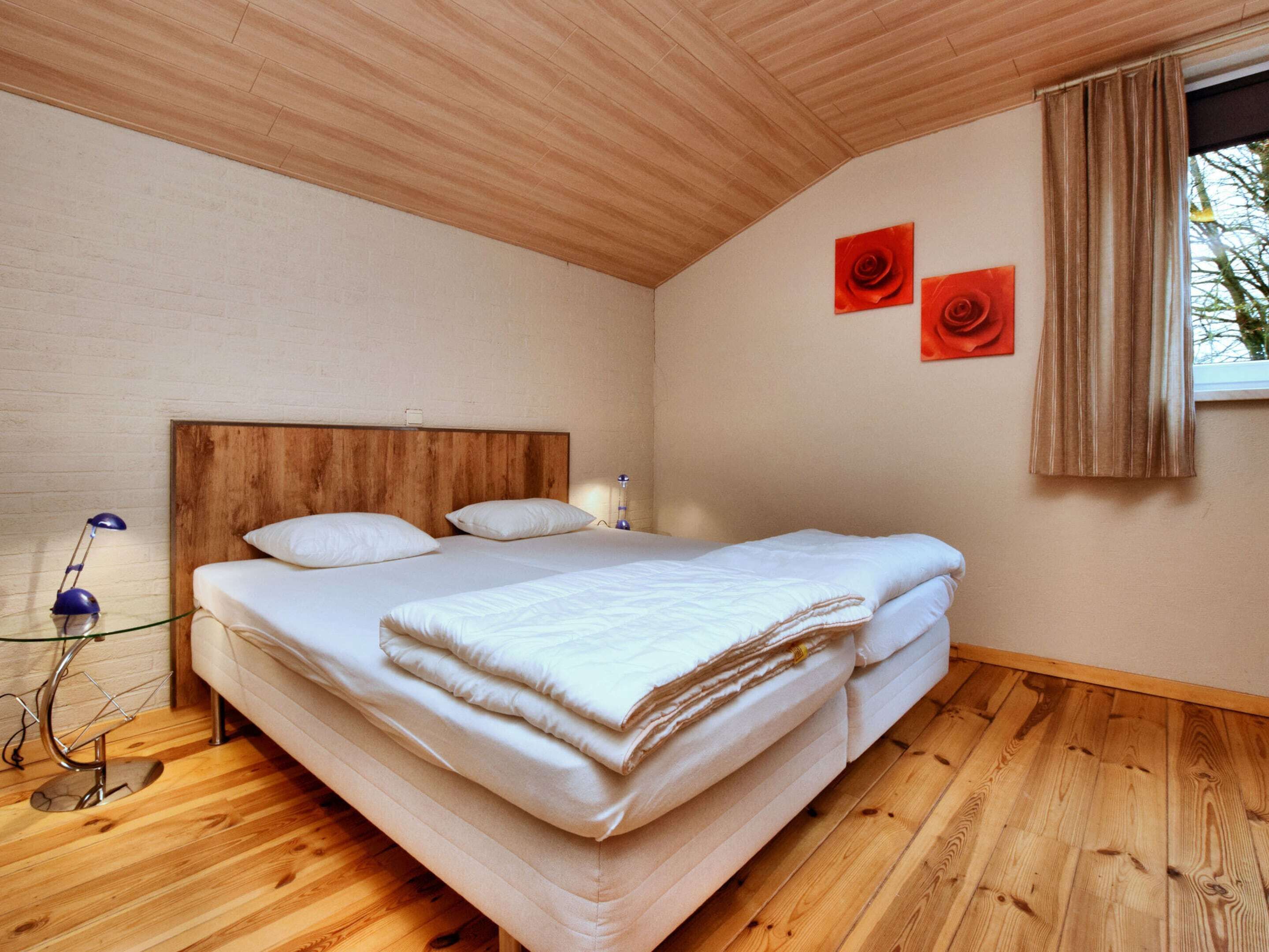 Ein Schlafzimmer mit Holzboden, einem Bett mit weißer Bettwäsche, einem Nachttisch mit Lampe und zwei Bildern von roten Rosen an der Wand.