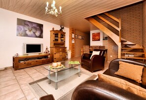 Un salon comprenant un téléviseur, un meuble en bois, une table basse en verre, un canapé en cuir et un escalier.