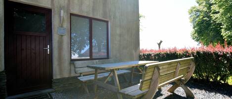 A wooden bench and picnic table outside a building with a door and window.
