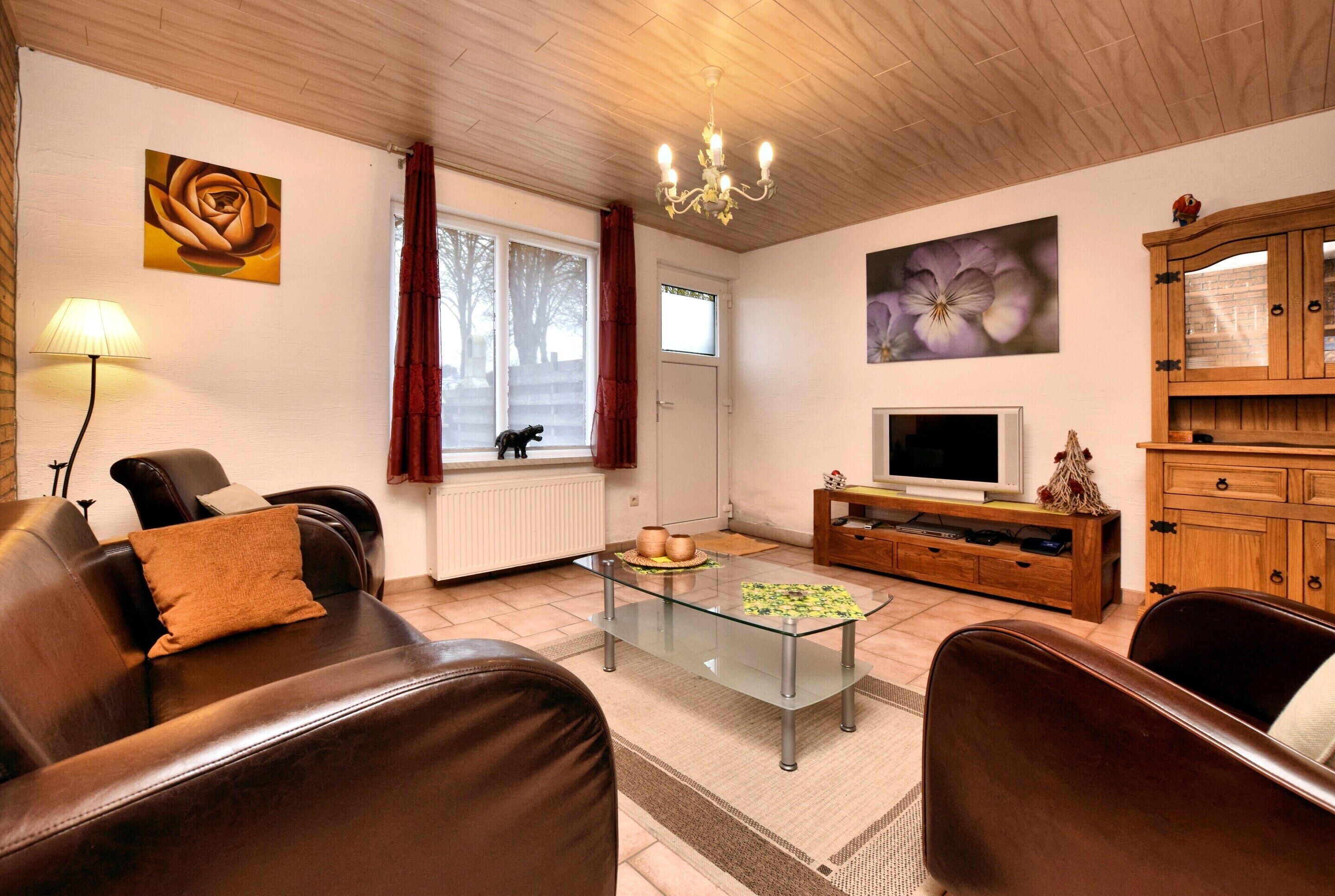 Un salon avec un canapé en cuir marron, une table basse en verre, un téléviseur posé sur un meuble en bois et un lustre.