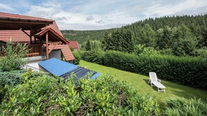 A wooden cabin with a red roof, a blue awning, and a white lounge chair in the yard. - Sunny Terrace & Quiet Stay (Friedrichroda)