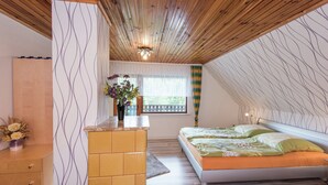 A bedroom with a sloped ceiling, a bed with green bedding, a dresser, and a window with a view of greenery. - Sunny Terrace & Quiet Stay (Friedrichroda)