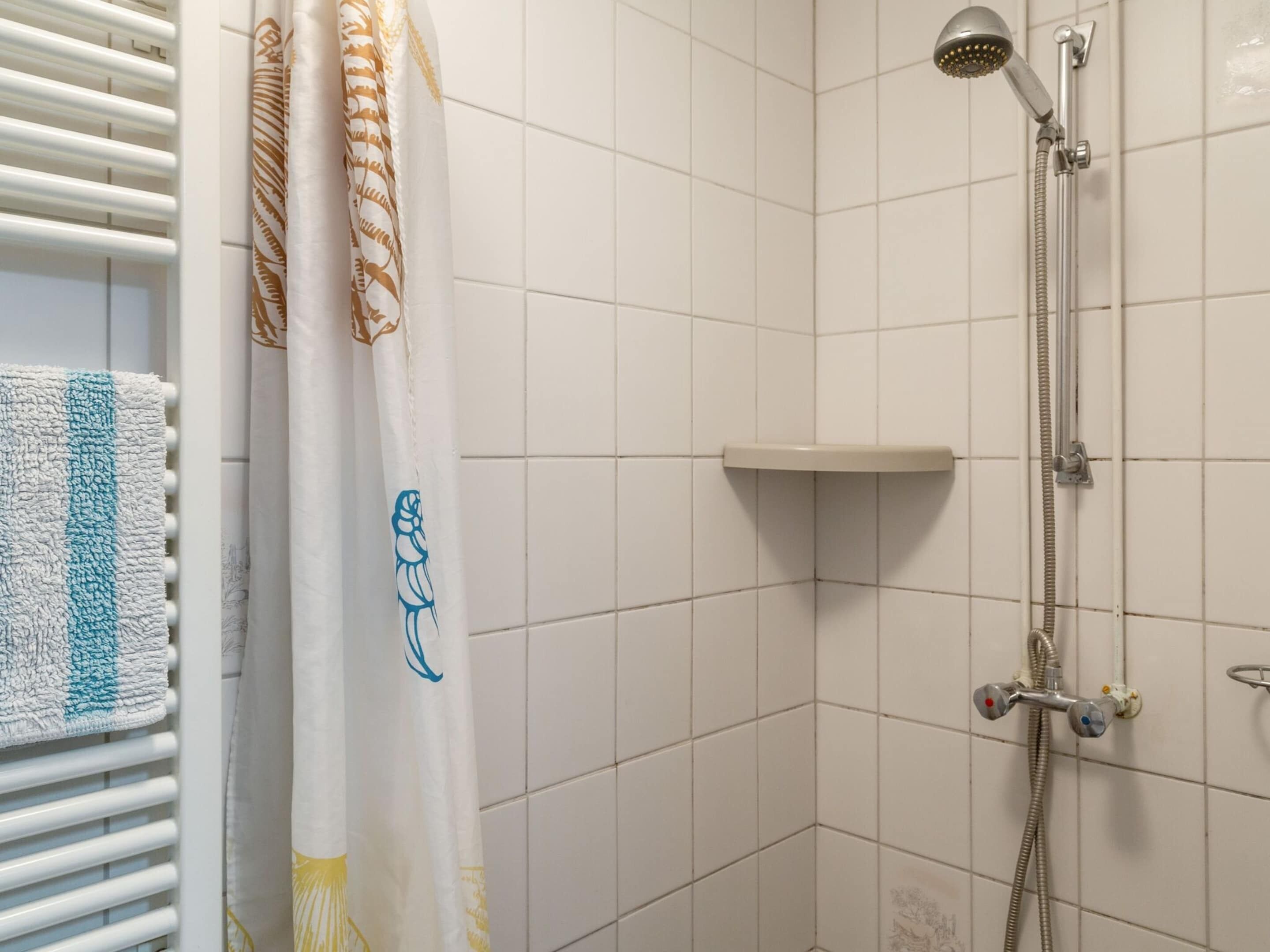 Zona de ducha con cabezal de ducha de mano, grifo de pared y toallero con una toalla.