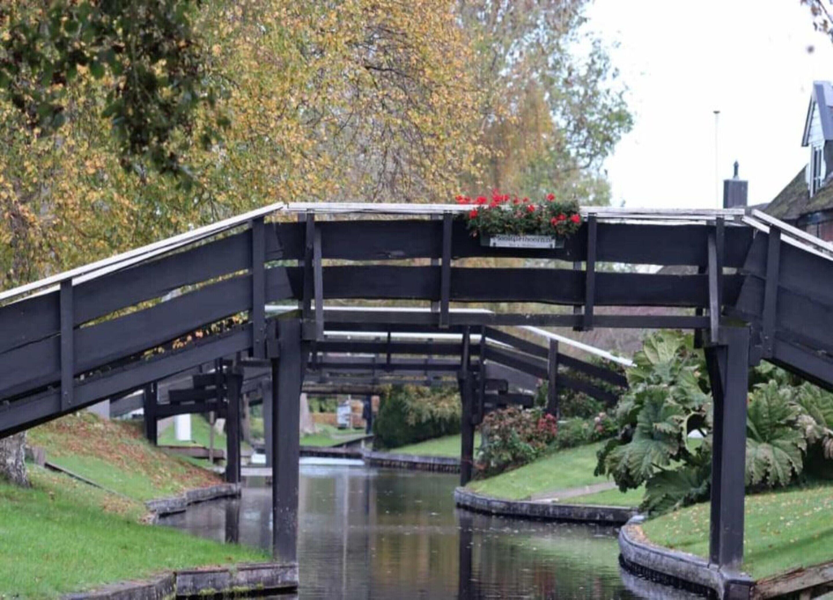 A black metal bridge over a canal with a flower bed on top and a building in the background.