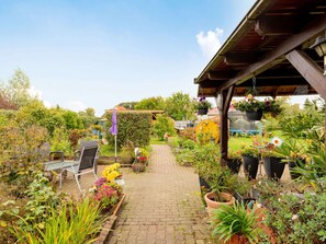A garden pathway leading to a covered seating area with chairs and tables, surrounded by various potted plants and flowers. - Wohnung im OT Brusow mit Garten (Kroepelin)