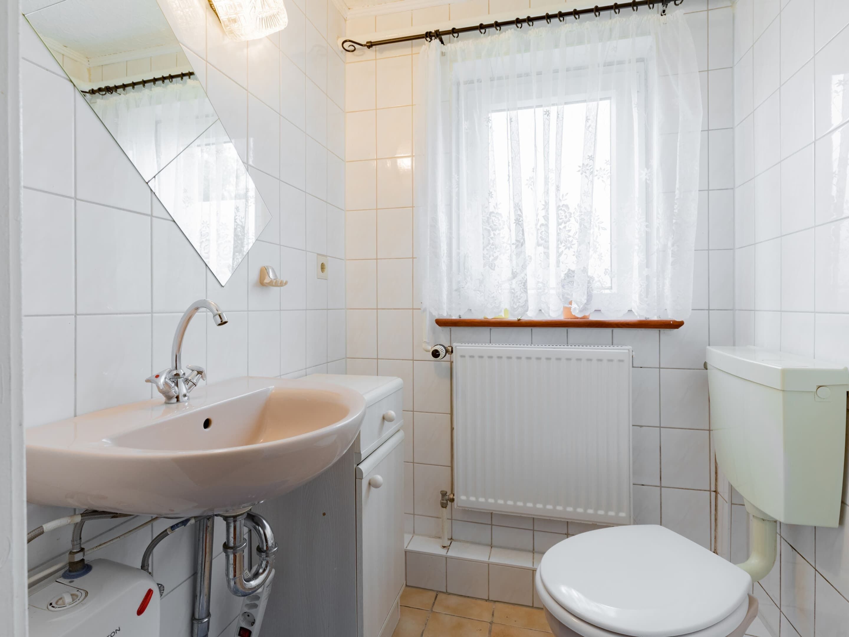 Ein Badezimmer mit Waschbecken, Toilette und einem Fenster mit Vorhang.