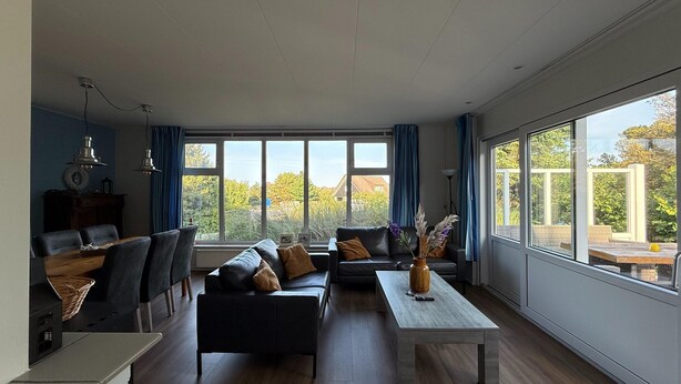 A spacious living room with a dining area, large windows, and a view of the outdoors.