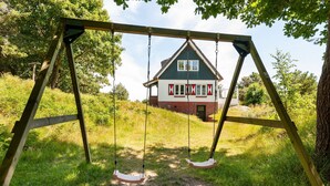 A wooden swing set in a grassy area with a house in the background.