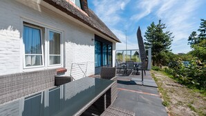 A modern house with a white exterior, a thatched roof, and a patio area with a glass table and wicker furniture.