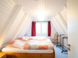 Un dormitorio acogedor en el ático, con una cama de madera, una ventana con cortinas rojas y una lámpara en el techo.
