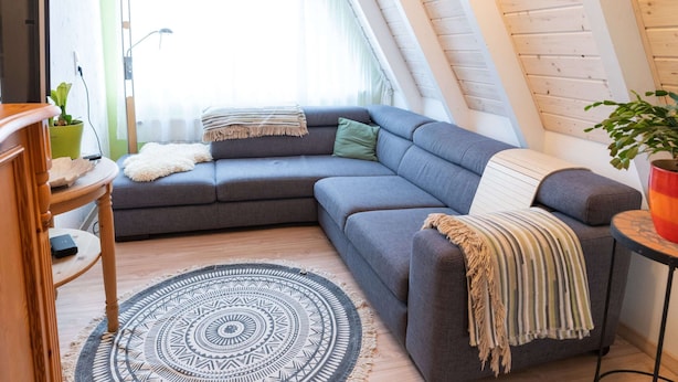 Un coin douillet avec un canapé d’angle gris, un tapis à motifs et une petite table en bois sur laquelle est posée une plante.