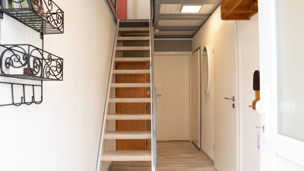A narrow hallway with a wooden staircase leading to a door. - Ferienhaus in Bestwig mit Privatem Garten (Bestwig)
