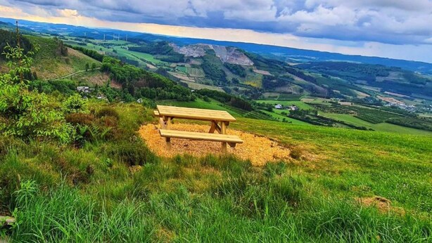 A picnic table on a grassy hill overlooking a valley with wind turbines in the distance. - Ferienhaus in Bestwig mit Privatem Garten (Bestwig)