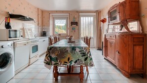 Een keuken met een eettafel, houten kastjes, een wasmachine en een magnetron.