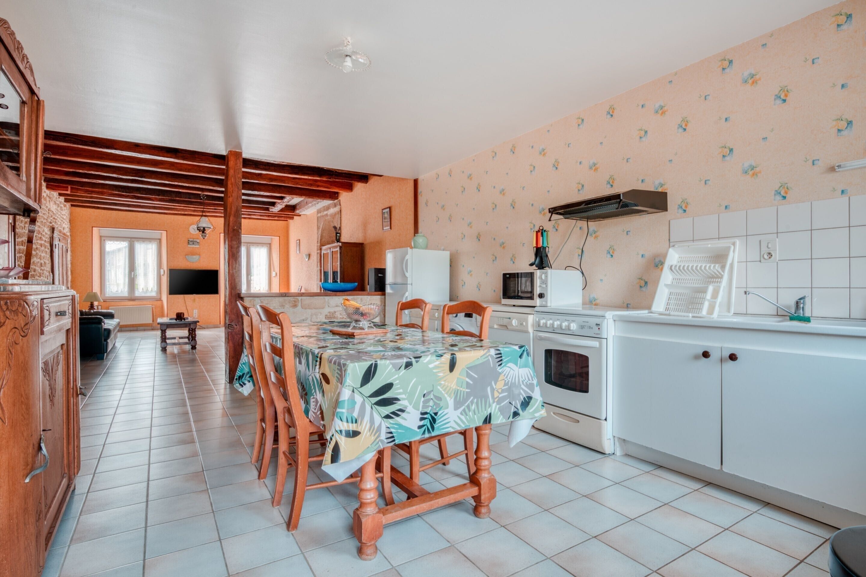 A spacious kitchen with wooden cabinets, a dining table with a tropical leaf-patterned tablecloth, and a tiled backsplash.