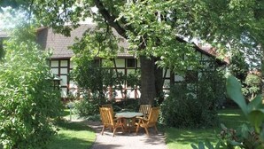A garden with a table and chairs under a tree, a pathway, and a building with a tiled roof. - Wohnung in Tabarz Thuringen in Waldnahe (Tabarz)