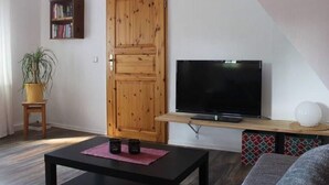 A living room with a wooden door, a bookshelf, a TV on a wooden stand, a small table with two cups, and a potted plant. - Wohnung in Tabarz Thuringen in Waldnahe (Tabarz)