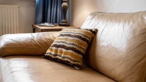 A leather sofa with a striped pillow, a table lamp, and a window with curtains in the background. - Apartment in Lennestadt for 2 Person (Lennestadt)
