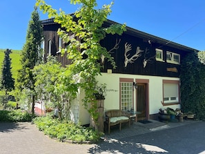 A two-story building with a garden, a wooden bench, and a door with a window.