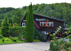 Ein traditionelles Holzhaus mit einem Schild, auf dem "Bergstübli" steht. Vor dem Eingang befindet sich eine Treppe, umgeben von üppigem Grün und einem gepflegten Garten.