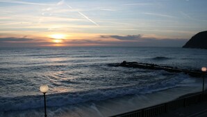 A sunset over the ocean with waves crashing onto the shore, a rocky outcrop on the right, and a walkway with street lamps. - Peaceful Countryside Retreat (Sesta Godano)