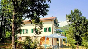 A two-story house with a balcony, a covered patio with chairs, and a stone wall. - Peaceful Countryside Retreat (Sesta Godano)