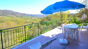 A balcony with a blue umbrella, white plastic chairs, and a view of a green valley. - Peaceful Countryside Retreat (Sesta Godano)