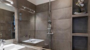Une salle de bain moderne avec une douche à parois de verre, deux lavabos et un grand miroir.