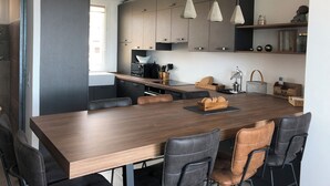 Une cuisine moderne avec une table à manger en bois, des chaises noires et marron, et des luminaires suspendus.