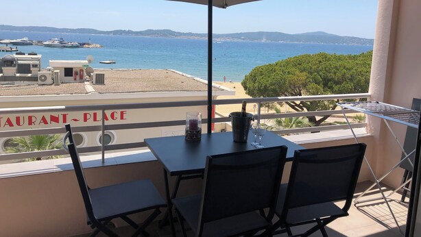 Un balcon avec une table, des chaises et un grand parasol, offrant une vue sur une plage et la mer.