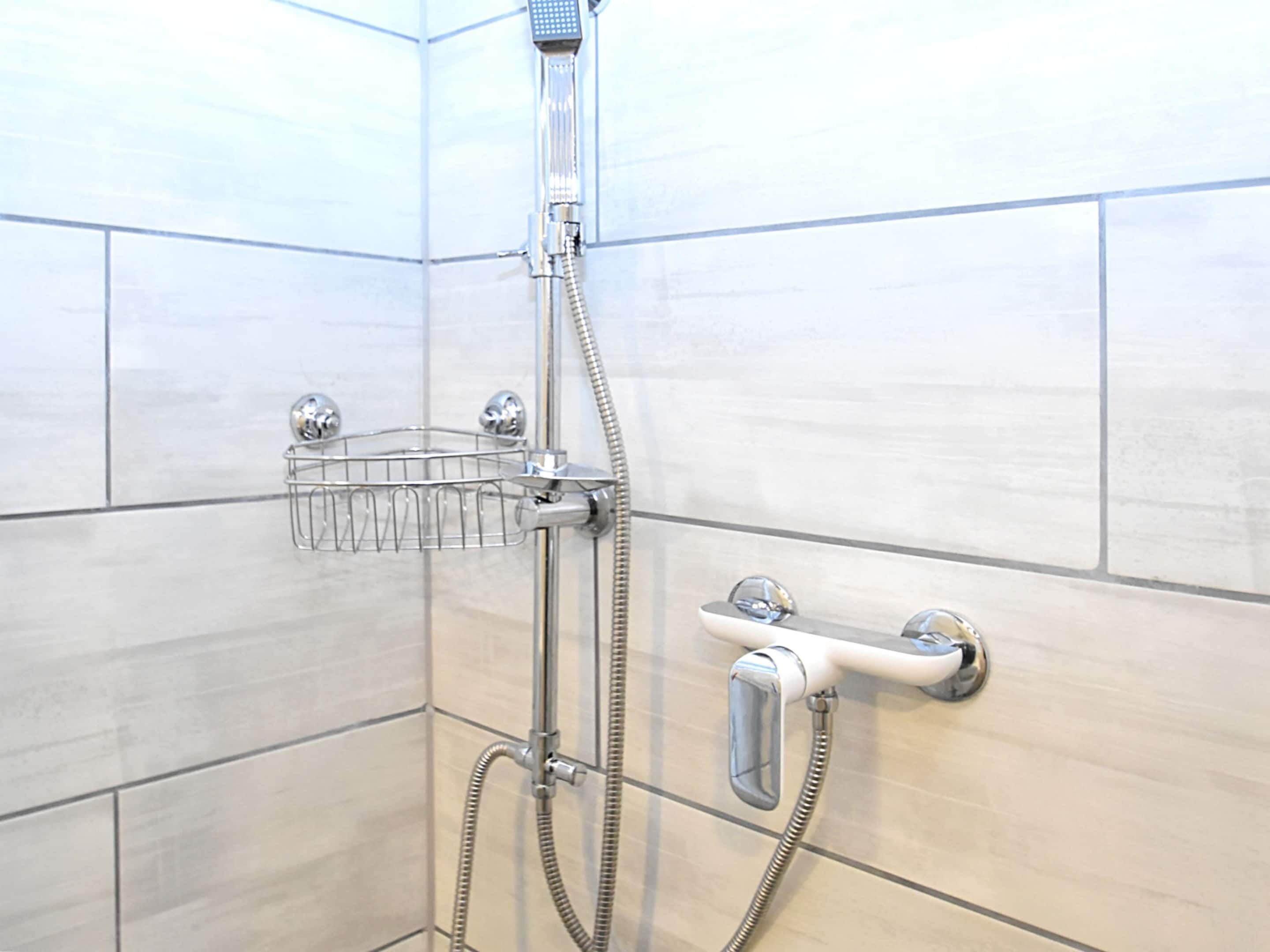 A shower with a chrome hose, a chrome showerhead, and a chrome shower control.