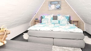 Une chambre avec un plafond en pente, un lit avec de nombreux oreillers, une table de chevet et une horloge murale.