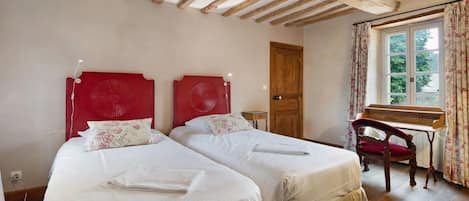 Una habitación con dos camas, un escritorio de madera, una silla y un ventanal con cortinas.