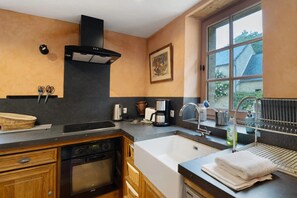 Una cocina con horno empotrado, lavamanos, cafetera y ventana con vistas al exterior.