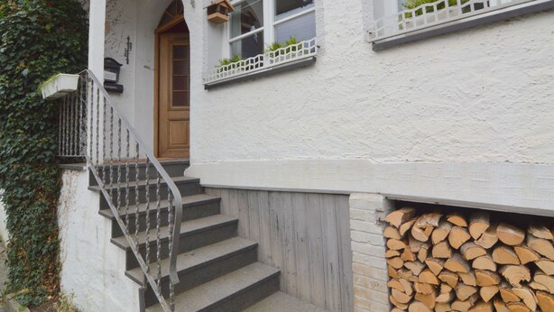 Ein weißes Gebäude mit einer Holztür, einer Treppe und einem Fenster mit weißem Geländer.