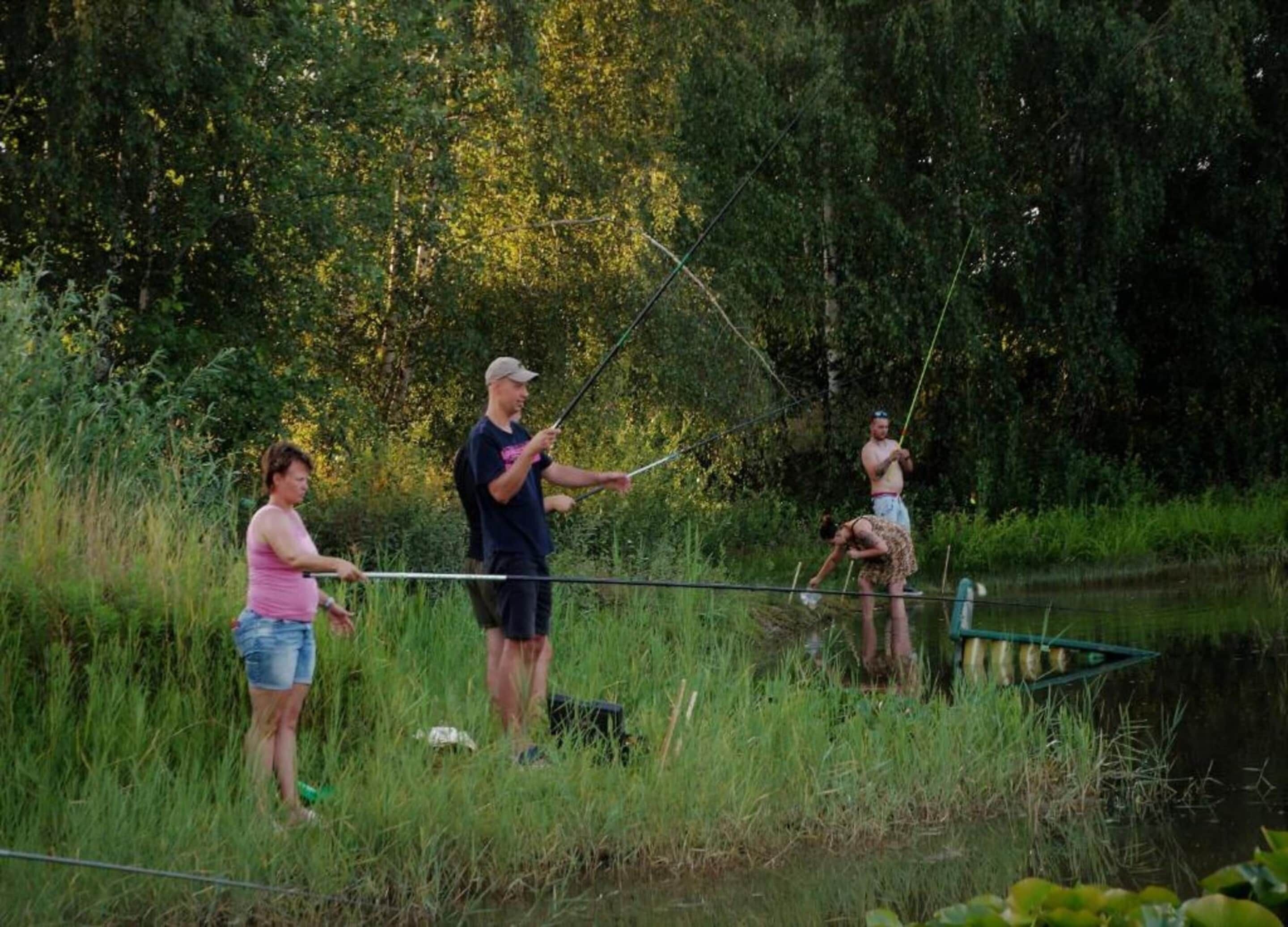 Three people fishing by a calm river surrounded by lush greenery.