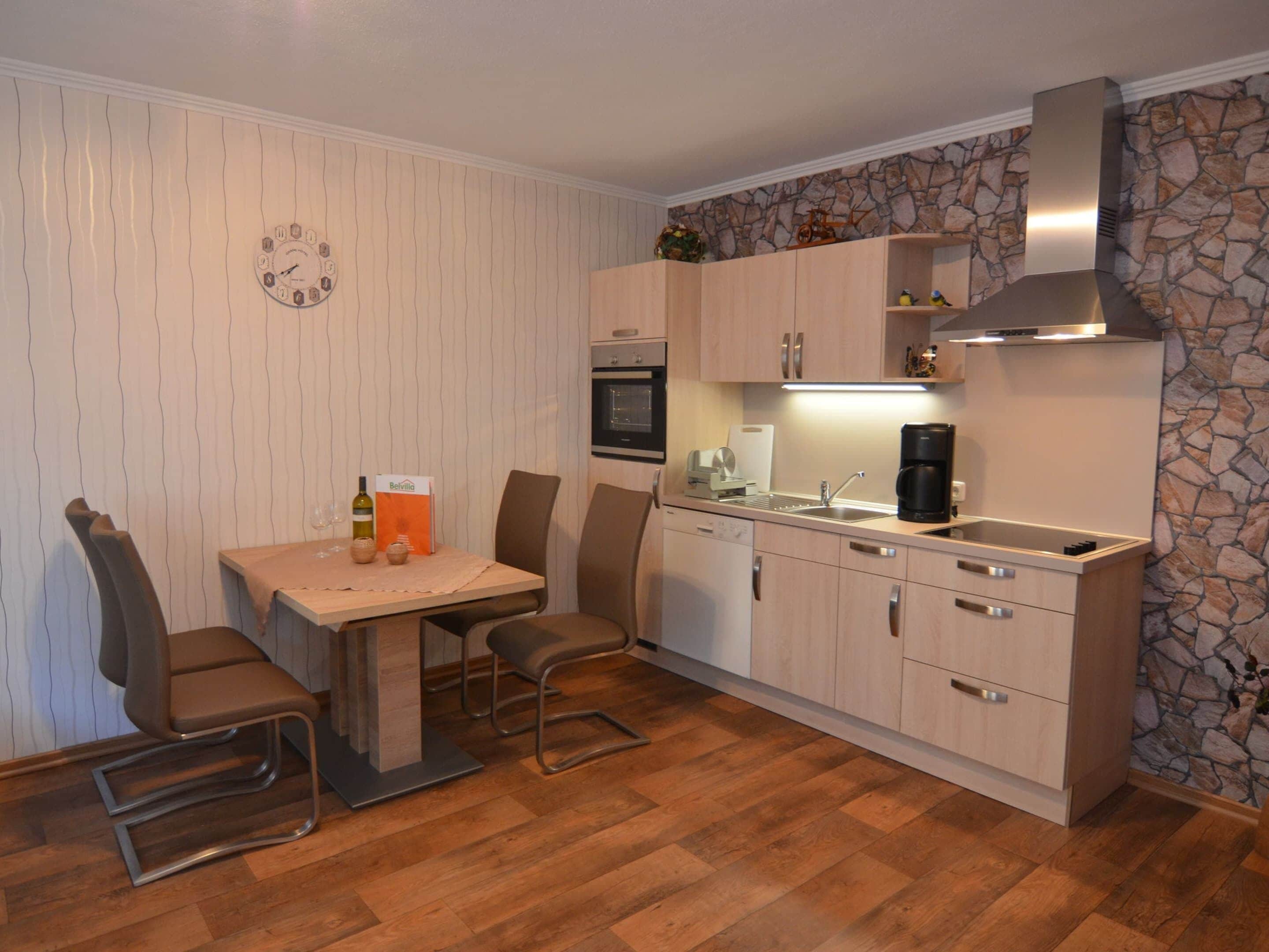 Een compacte keuken met een eethoek, met een accentmuur van steen, houten kasten en een inbouwoven.