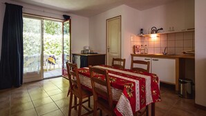 Een eetgedeelte met een tafel voor vier personen, een keuken met een betegelde spatwand, en een schuifdeur naar een buitenruimte.