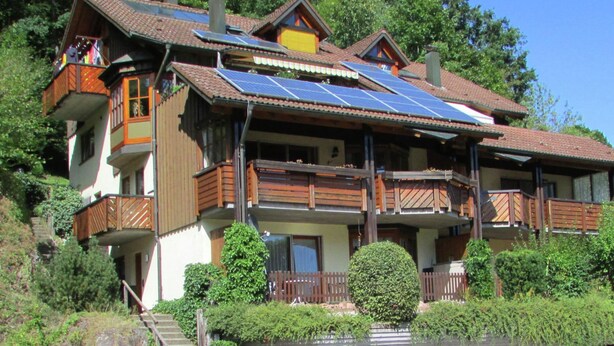 Una casa de dos pisos con techo inclinado, balcones de madera y paneles solares.