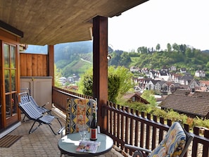 A balcony with two lounge chairs, a table with a bottle and glasses, and a view of a village with traditional houses. - Ferienwohnung in Schiltach (Schiltach)
