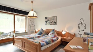 Un dormitorio con cama de madera, una mesita de noche, un escritorio, una silla, una ventana con cortinas, una lámpara colgante y decoración en la pared.