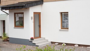 A modern building with a white facade, a wooden door, and a small porch with steps leading to the entrance. - Charming Home in Winterstein (Waltershausen)